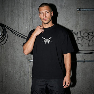 Zwart Tribal Techno Vibes oversized T-shirt, vooraanzicht bij model voor betonmuur #farbe_schwarz
