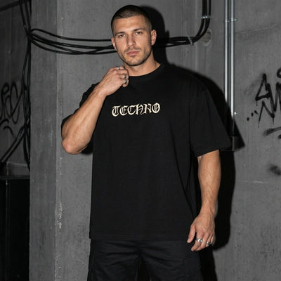 Zwart Techno Vibe oversized T-shirt, vooraanzicht bij model voor betonmuur